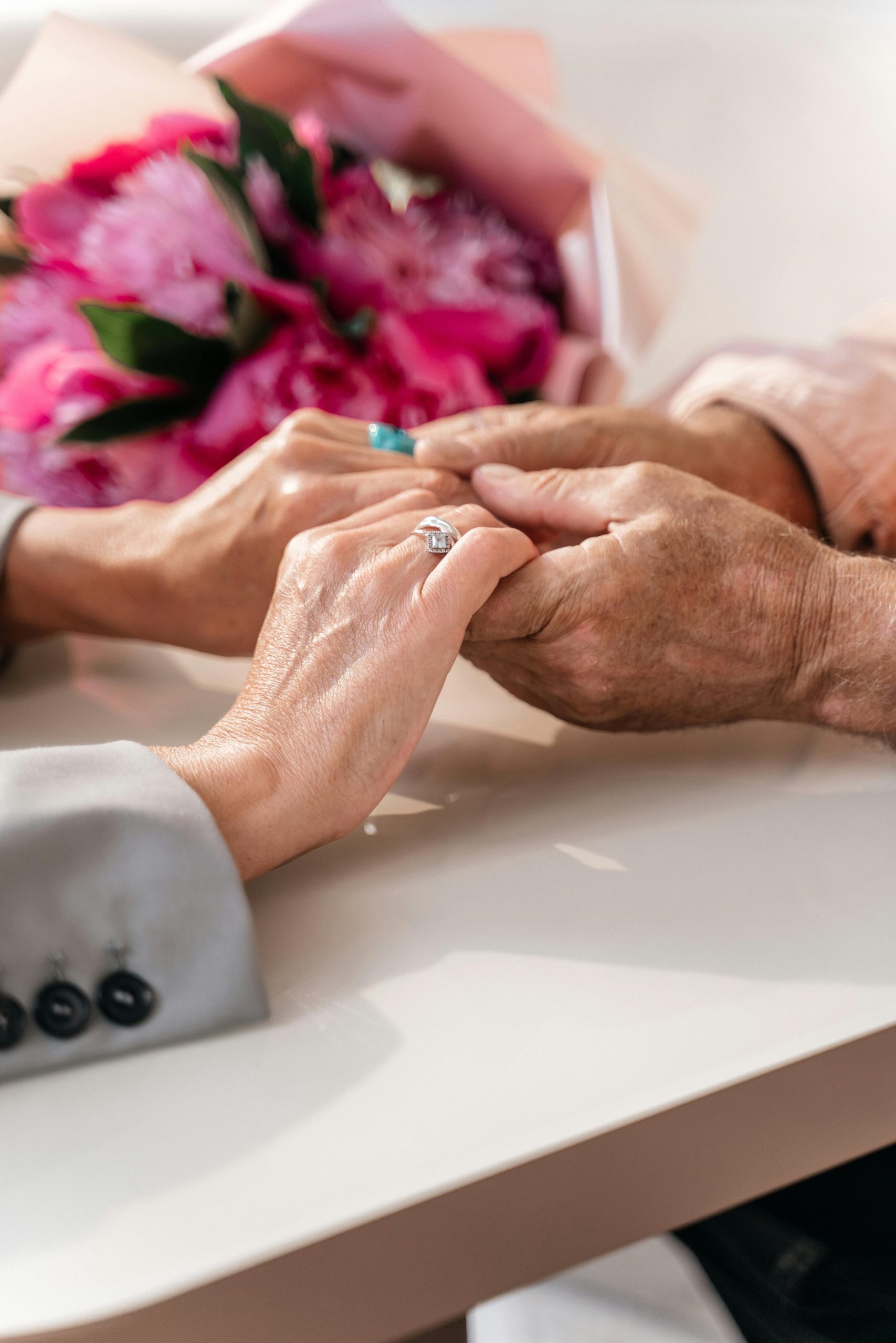 wo sets of elderly hands gently holding across a table — capturing emotional support, companionship, and meaningful connection in a senior living environment in East China, Michigan.